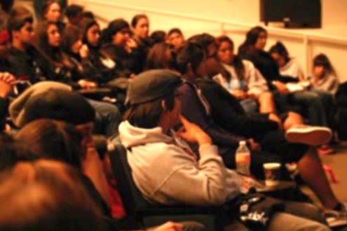 A group of people sitting in a lecture hall style room, watching and listening to a speaker off camera