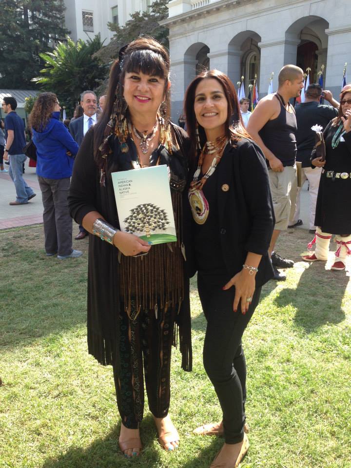 Dr. Joely Proudfit, CICSC Director, standing outside with another woman who is holding a copy of the State of American Indian and Alaskan Native (AIAN) Education in California Report 2014