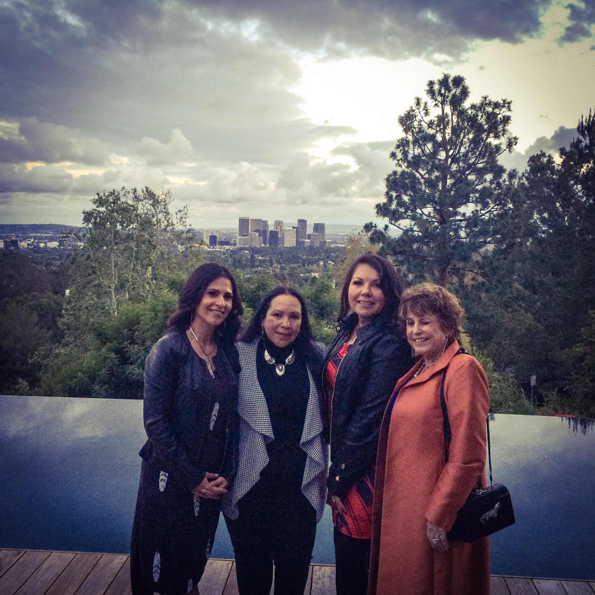 CSUSM Tribal Liaison Tishmall Turner and CICSC Director Dr. Joely Proudfit standing with two other women in front of an infinity pool that overlooks trees and a metropolitan city in the distance