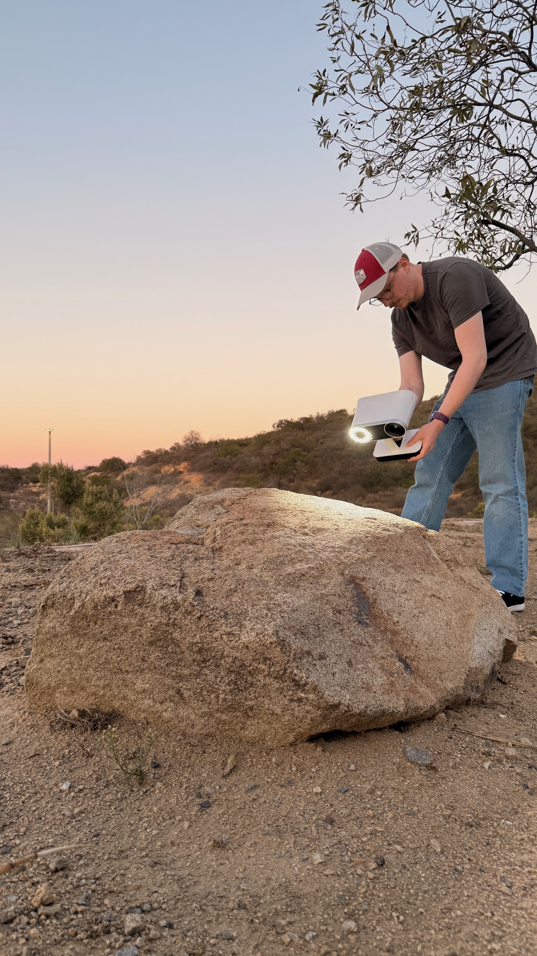 A person standing outside pointing an instrument at a boulder