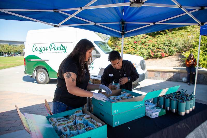 two volunteers preparing a table for a Cal Fresh event with Cougar Pantry van in the background
