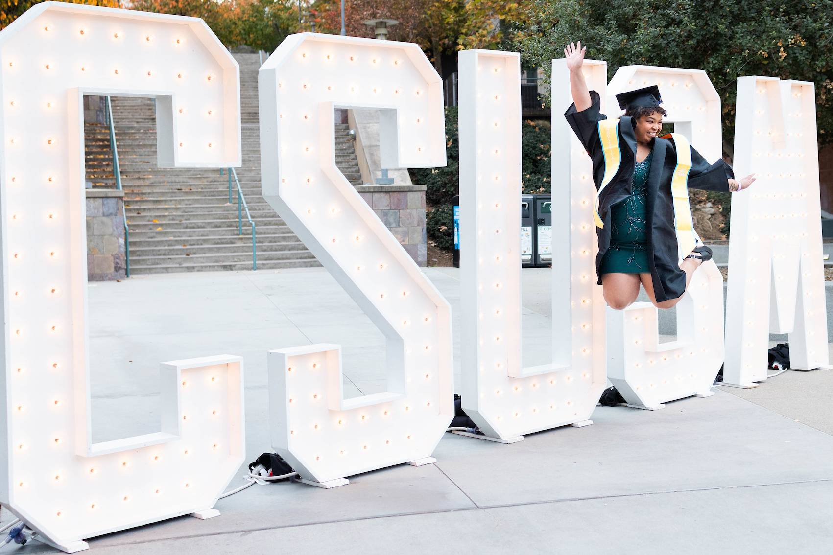 CSUSM grad jumping in front of CSUSM marquee letters