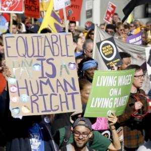 Image of protesters holding up signs that say "Equitable Pay is a Human Right".