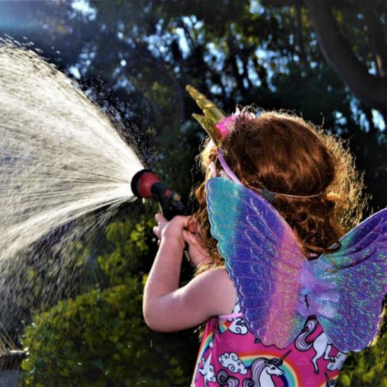 child with rainbow wings spraying water from a hose