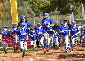 Little league team in blue uniforms running onto the field.