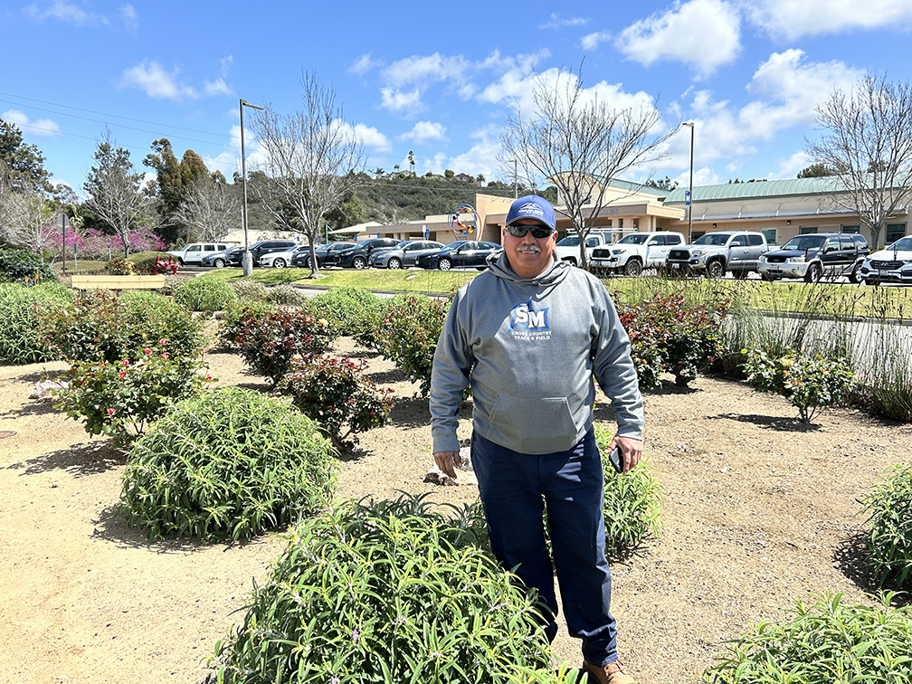 Man with sunglasses standing next to bushes
