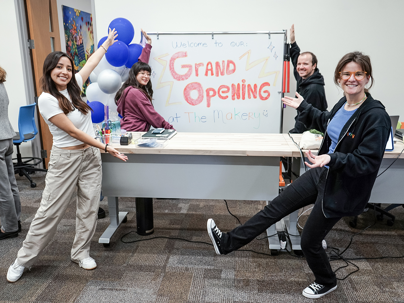 Four people pointing to a sign that says grand opening.