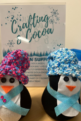 Crafted penguins in front of Crafting and Cocoa flyer