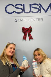 Two poeple posing witht heir crafted gnomes in front of the Staff Center logo
