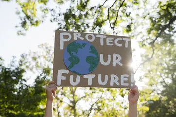 Hands holding a sign that reads protect our future with an image of Earth